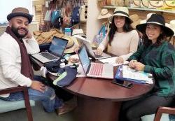 Three students wearing hats sitting at table discussing fashion merchandising