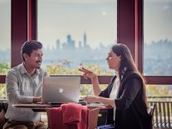 Graduate students talk to one another with New York City skyline in the distance.