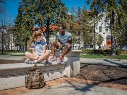 Two students laughing outside with each other on a sunny day outside of a college building.