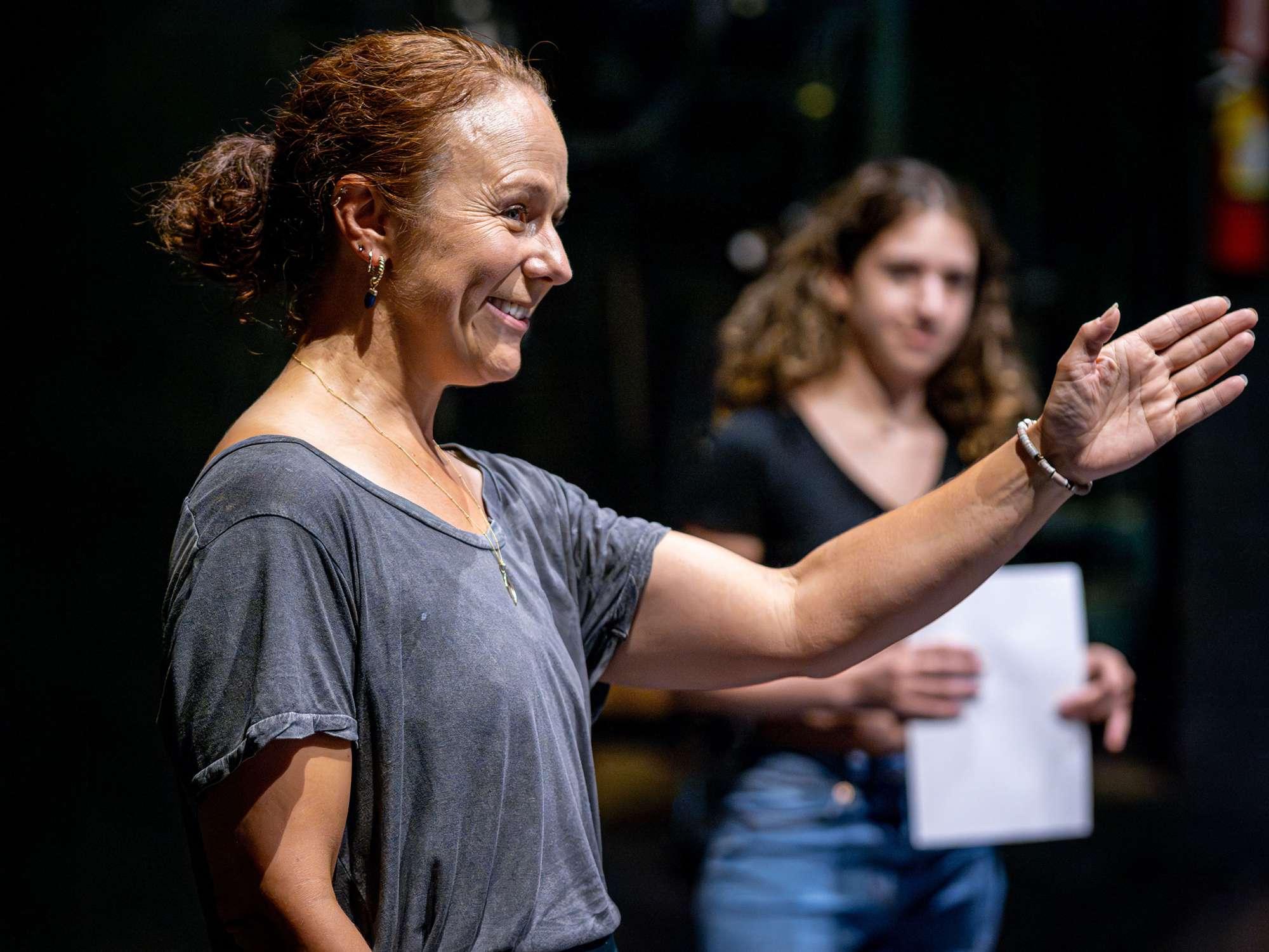 An smiling acting teacher gestures to students.