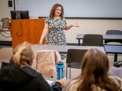 A woman stands in front of students, gesturing.