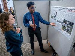 Richard Steiner-Otoo gestures while discussing his research poster at a symposium.