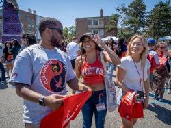 Two Montclair State University students and one Bloomfield College student stand together, chatting at an outdoor carnival.