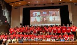 A group of people in three rows on a stage in red t-shirts.