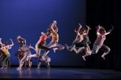 Photo of large group of dancers in formation and jumping.