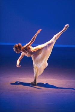 Photo of single dancer in leg-lift pose in spotlight.